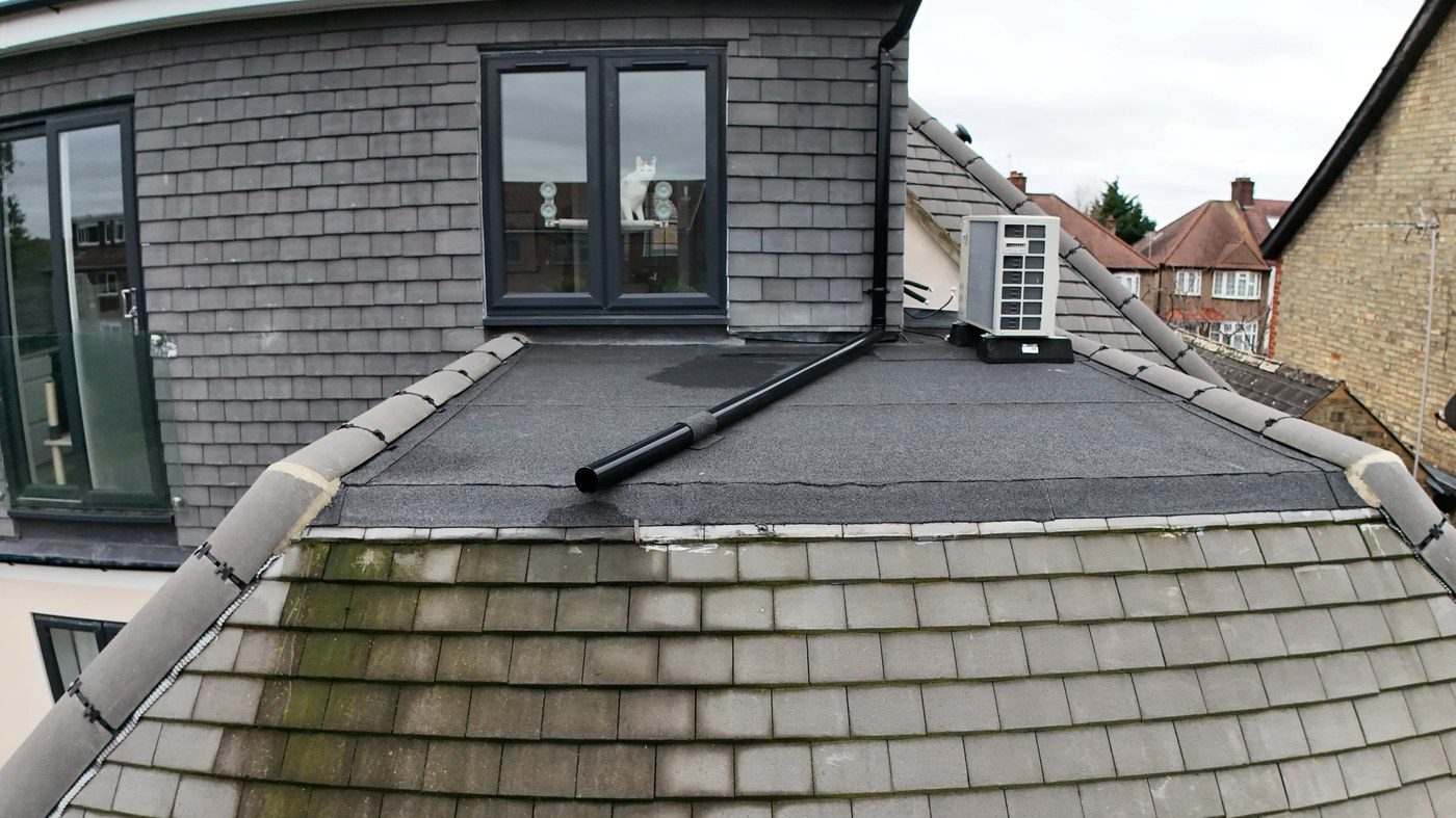 Close view showing early moss growth on lower hip tile courses and tile-to-flat-roof junctions